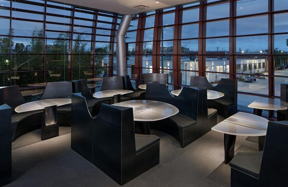 Modern office lounge with sleek black furniture, curvy designs, and large windows overlooking an evening cityscape.